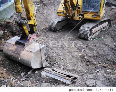 A yellow and black construction machine is digging a hole in the dirt A yellow and black construction machine is digging a hole in the dirt 125998714