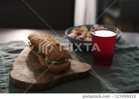 Baguette sandwich with jamon, mozzarella and salad leaves with bowl of salad and glass of lemonade for lunch on dining table Baguette sandwich with jamon, mozzarella and salad leaves with bowl of salad and glass of lemonade for lunch on dining table 125999918