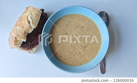 Bowl of creamy soup served with a crusty sandwich on a white background. Concept of homemade comfort food, warm lunch and simple rustic meal Bowl of creamy soup served with a crusty sandwich on a white background. Concept of homemade comfort food, warm lunch and simple rustic meal 126000016