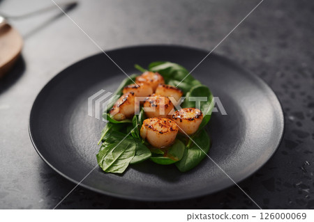 Seared scallops on pile of spinach on black plate closeup Seared scallops on pile of spinach on black plate closeup 126000069