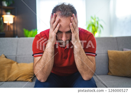 Man sitting alone at home looking sad and distraught Man sitting alone at home looking sad and distraught 126000527