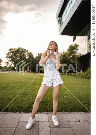 Portrait of beautiful blonde woman with white headphones in outdoor 126000534