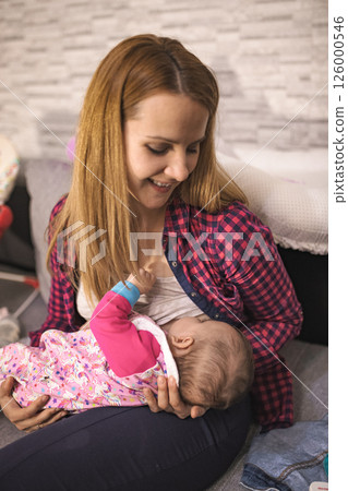 Mother breastfeeding her baby at home in a cozy living room Mother breastfeeding her baby at home in a cozy living room 126000546