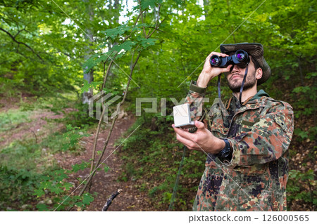 Soldier exploring forest using binoculars and compass for navigation 126000565