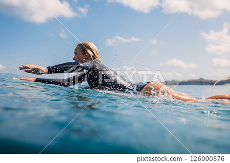 Beautiful woman surfer paddling on surfboard through crystal clear water Beautiful woman surfer paddling on surfboard through crystal clear water 126000876