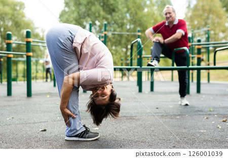Mature woman doing yoga outdoors in city sports ground 126001039