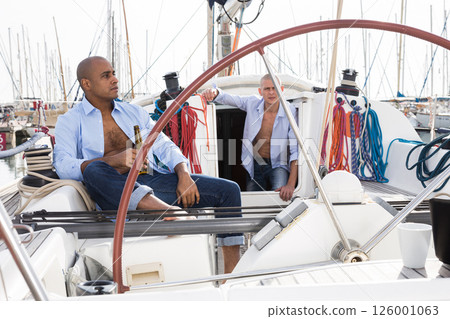 Two men in blue shirts relaxing on sailing yacht in the port Two men in blue shirts relaxing on sailing yacht in the port 126001063