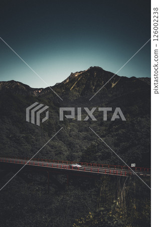 一輛跑車駛過一座紅色的橋,背景是雄偉的山脈 一輛跑車駛過一座紅色的橋,背景是雄偉的山脈 126002238