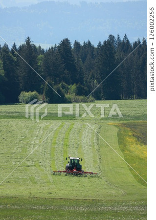 A tractor is driving down a field of grass A tractor is driving down a field of grass 126002256