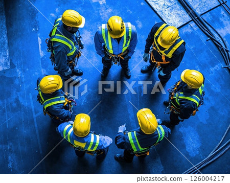 Construction team safety briefing: workers in yellow helmets at industrial site in blue tones Construction team safety briefing: workers in yellow helmets at industrial site in blue tones 126004217