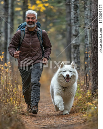 Autumn adventure: mature man and fluffy white dog enjoying a vibrant forest hike in nature's tranquility Autumn adventure: mature man and fluffy white dog enjoying a vibrant forest hike in nature's tranquility 126004375