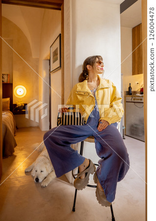 Stylish woman in yellow jacket sitting indoors with large dog resting nearby 126004478