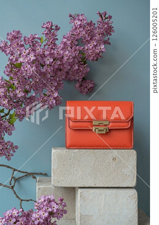 Elegant spring design with orange bag and purple blossoms for fashion and floral concept Elegant spring design with orange bag and purple blossoms for fashion and floral concept 126005201