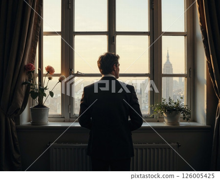 Cityscape reflection: elegant businessman contemplating urban life at sunrise from high-rise window 126005425