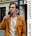 Urban elegance: stylish man in mustard jacket taking a phone call 126005634