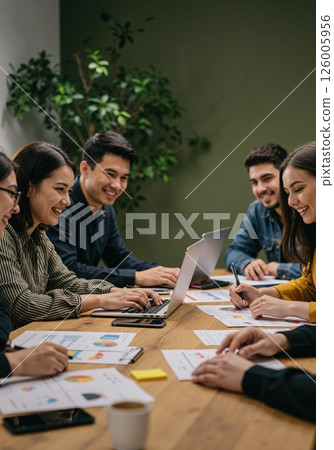 Collaborative team meeting with laptops and graphs in modern office setting 126005956