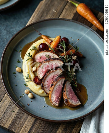 Gourmet plated duck breast with carrot, grape, and herb garnish on wooden board 126006613