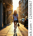 Urban sunset stroll: young woman in city street with golden light reflections 126006867