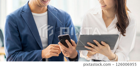 Male and female businessmen talking while looking at a tablet and smartphone Male and female businessmen talking while looking at a tablet and smartphone 126006955