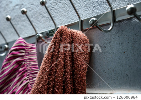Striped and brown towels hanging on metal hooks by a textured wall 126006964