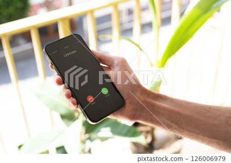 Fraud or fraudulent schemes. Close-up of a male hand holding a phone with an unexpected incoming call from an unknown 126006979