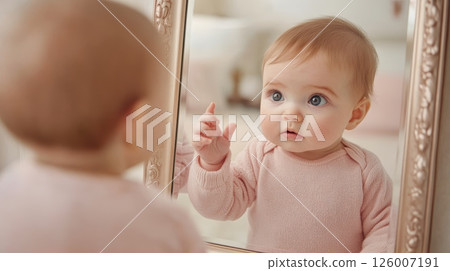 A curious baby observes its reflection in a mirror, captivated by the sight in a cozy room 126007191