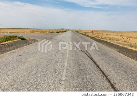 Straight asphalt road stretches through flat arid landscape in Atyrau Region Kazakhstan Straight asphalt road stretches through flat arid landscape in Atyrau Region Kazakhstan 126007348