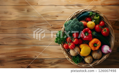 Top view of a wicker basket filled with fresh vegetables on a wooden kitchen counter 126007498