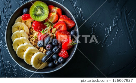 A round plate of granola and mixed fruits on a black table, with copy space 126007927