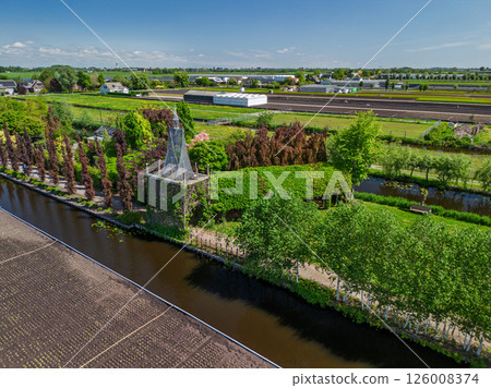 Aerial view of a lush countryside garden surrounded by canals and farmlands, with a cozy house and colorful trees, set in a peaceful rural landscape under a clear blue sky. Aerial view of a lush countryside garden surrounded by canals and farmlands, with a cozy house and colorful trees, set in a peaceful rural landscape under a clear blue sky. 126008374