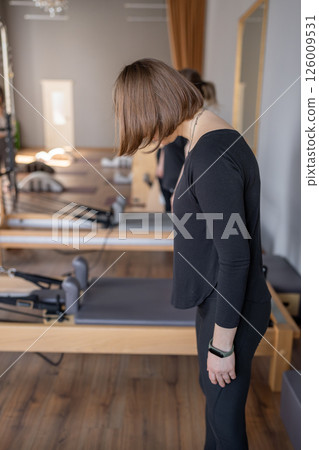 Young caucasian woman doing roll down exercise in a pilates bright studio. Their workout focuses on core strength and flexibility in a modern fitness environment. Young caucasian woman doing roll down exercise in a pilates bright studio. Their workout focuses on core strength and flexibility in a modern fitness environment. 126009531