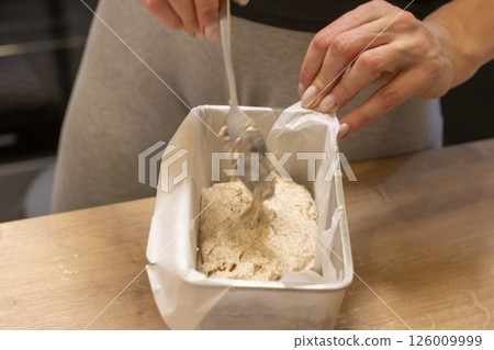 Woman adding ingredients together to prepare dough 126009999