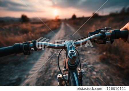 Hand holding bicycle handlebars on road at sunset 126010111