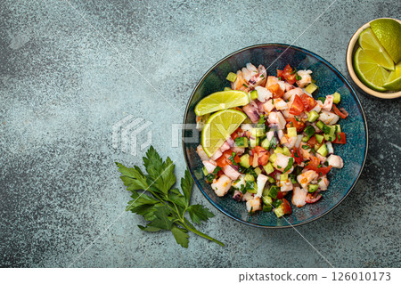 Peruvian seafood ceviche with shrimps, octopus, tomatoes, cucumber, and parsley in a bowl served with lime top view, space for text 126010173