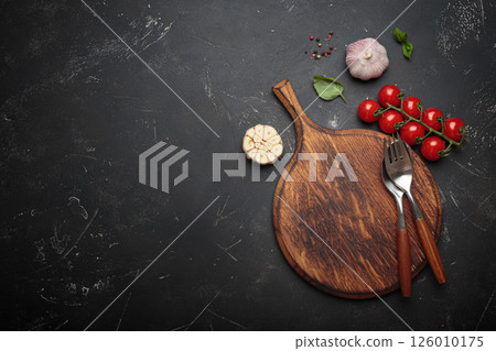 Food background with fresh vegetables, cooking ingredients, spices resting on rustic wooden cutting board, black background, space for text 126010175