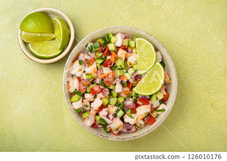 Peruvian seafood ceviche with shrimps, octopus, tomatoes, cucumber, and parsley in a bowl served with lime top view 126010176