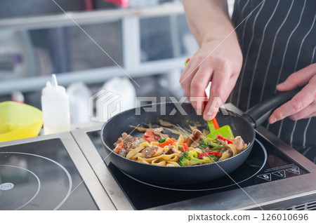 The chef cooks pasta in a frying pan.  126010696