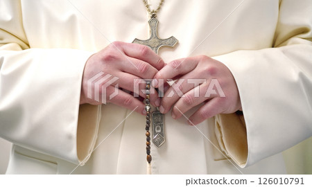 Medium close up of unrecognizable hand of priest holding rosary with cross 126010791