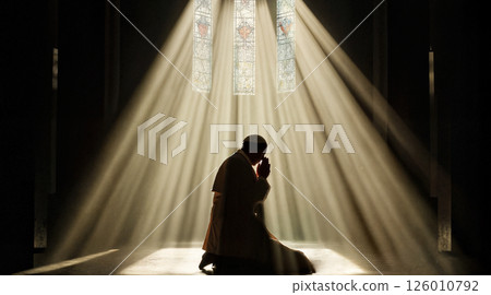A silhouette of the Pope kneeling in prayer inside a vast, dimly lit cathedral. 126010792