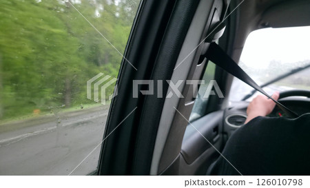 Driving in the rain. Interior view from the passenger seat. Wet window, blurred scenery. Focus on safety belt. Travel, transportation concept. Driving in the rain. Interior view from the passenger seat. Wet window, blurred scenery. Focus on safety belt. Travel, transportation concept. 126010798