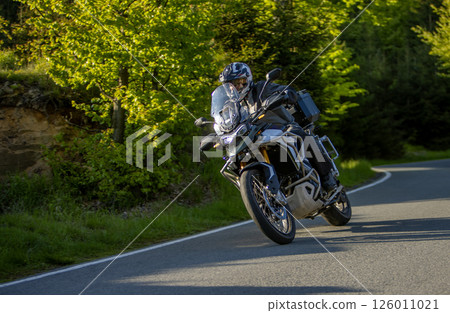Driver riding motorcycle on empty asphalt road, blurred motiion, spring mountains Driver riding motorcycle on empty asphalt road, blurred motiion, spring mountains 126011021
