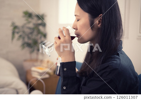 A woman in her 40s drinking wine at home during the day 126011307