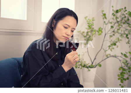 A woman in her 40s drinking wine at home during the day A woman in her 40s drinking wine at home during the day 126011481