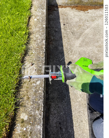 Male hands in green gloves cut a metal bolt protruding from a concrete beam with electric reciprocating saw. 126011583