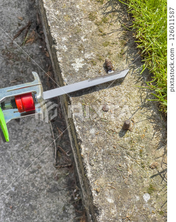 Male hands in green gloves cut metal bolt protruding from concrete beam with electric reciprocating saw. 126011587