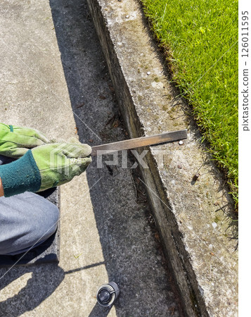 Male hands in green gloves file a metal bolt sticking out of a concrete beam. 126011595