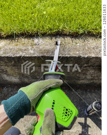 Male hands in gloves cut metal bolt protruding from concrete beam with electric reciprocating saw. 126011633