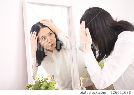 A middle-aged woman who is concerned about her hairline in the mirror A middle-aged woman who is concerned about her hairline in the mirror 126011688