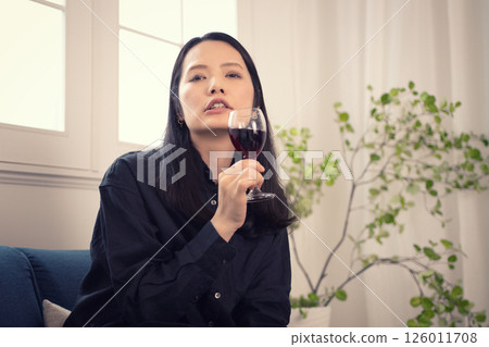 A woman in her 40s drinking wine at home during the day A woman in her 40s drinking wine at home during the day 126011708