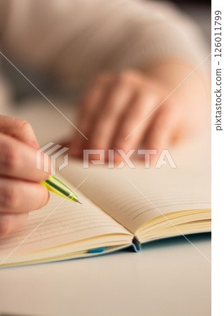 Close up image of human holding pen and writing something on blank white page in notebook. 126011799